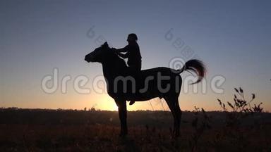 骑手坐在马上，在日落时给他两条腿。 慢动作。 剪影。 侧视图